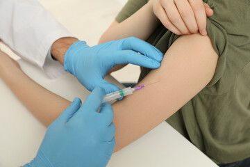 Doctor giving hepatitis vaccine to patient at table, closeup