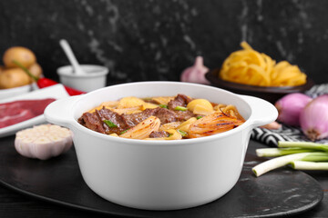 Pot of delicious vegetable soup with meat, noodles and ingredients on black wooden table