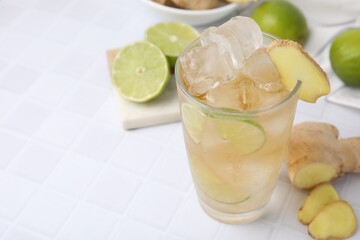 Glass of tasty ginger ale with ice cubes and ingredients on white tiled table, closeup. Space for text