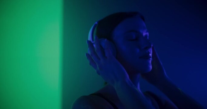 Creative Young Female Putting On Stylish Modern Headphones, Listening to Music in a Studio with Abstract Colorful Background. Beautiful Dancer Listening to the Beats, Expressing Her Joy Through Dance