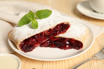 Delicious strudel with cherries, powdered sugar and mint on wooden table, closeup
