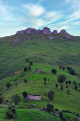 Fototapeta premium Small stone cottage in lush green countryside with hills under blue cloudy sky in Cantabria, Spain