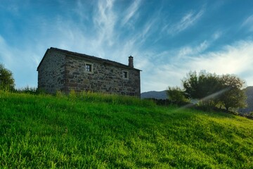 Fototapeta na wymiar Small stone cottage on the hill in lush green countryside under blue cloudy sky in Cantabria, Spain