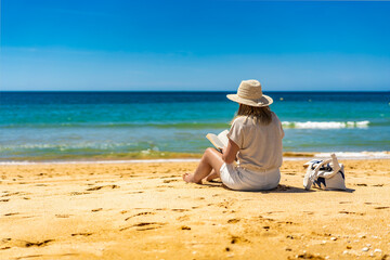 Woman sitting on beach in Alvor, Portugal reading book