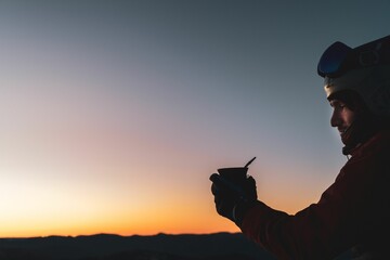 Closeup of a climber holding a cup against the background of the sky at sunset.