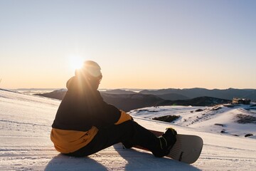Snowboarder sitting on the snowy ground at sunset