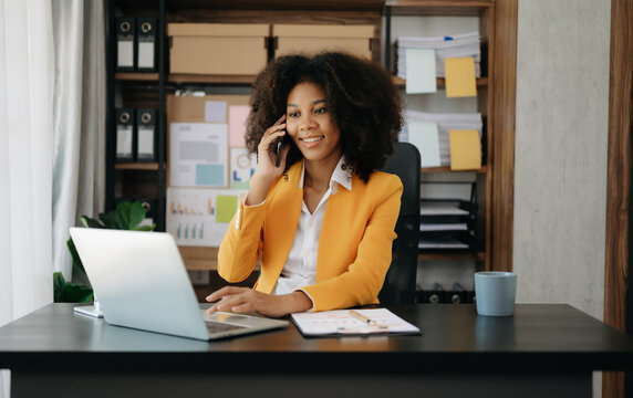 Business African woman Talking on the phone and using a laptop with a smile while sitting at office