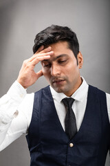 Indian young business man with stressed facial expressions in formal wear wearing white shirt, black tie, black coat against grey background. Male model.