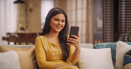 Indian Woman Using Video Call On Smartphone At Home: Doing Remote Work, Making Video Meetings with Clients. Young Woman Cherishing Video Calls with Her Boyfriend or Parents, Sharing Laughter and Love