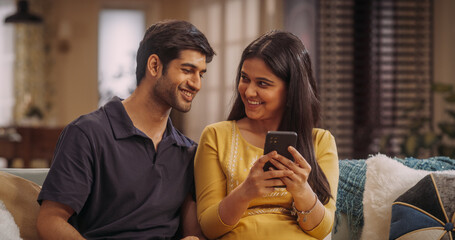 Indian Couple Using Smartphone At Home, Comparing Prices And Reviews On E-Commerce Sites. Discovering Best Deals On Fashion, Electronics, And Home Essentials While Enjoying Time Together.