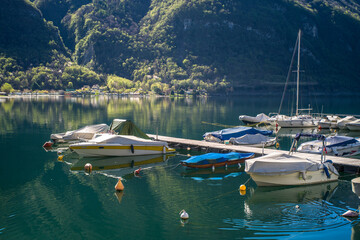 Lake Lugano surrounded by mountains and a small marina with moored boats on a sunny day
