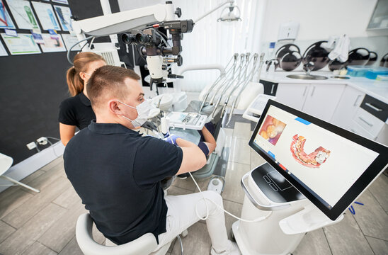 Dentist scanning patient's teeth with modern machine for intraoral scanning. Digital print of patient's teeth is on big screen. Modern high precision technologies. Concept of modern dentistry