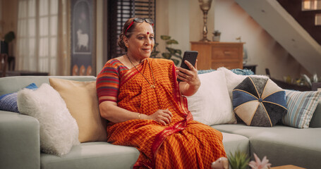 Obraz premium Elderly Woman Using Smartphone for Video Call: GreetingFriends, Sharing Joyful Moments, and Talking with Family Relatives. Embracing Technology to Stay Social and Active. Medium Shot.