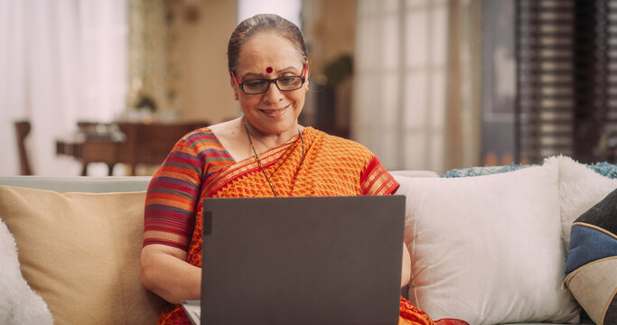 Elderly Indian Woman Using Laptop at Home: Enhancing Her Culinary Skills with Online Cooking Classes, Exploring New Recipes, Sharing Family Traditions. Granmother Eperiences Joy of Learning, Creating