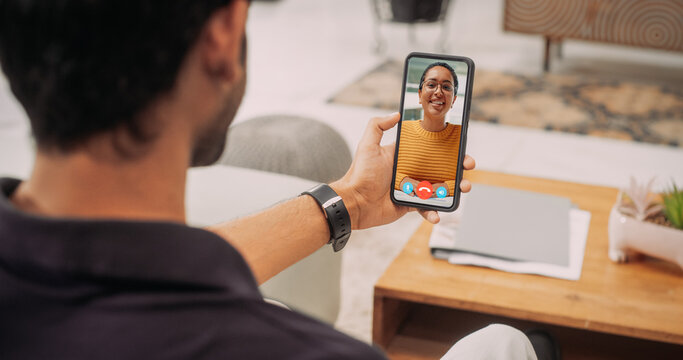 Over the Shoulder Indian Man Using Smartphone to Talk to his Long Distance Black Female Friend or Girlfriend Yousing a Video Call at Home. Young Male Having a Job Interview, Working Remotely 