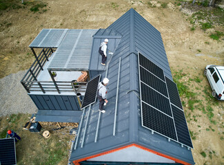 Men workers prepearing for mounting photovoltaic solar modules on roof of house. Electricians in...