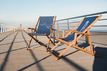 Closeup shot of two beach chairs on the wooden dock with a lighthouse in the background