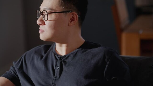 Pensive asian man in eyeglasses looking to side while sitting at home