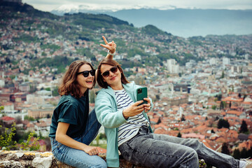 LGBT lesbian couple love moments together during travel vacation. Authentic people using smartphone against the background of a beautiful European city with orange roofs in the mountains
