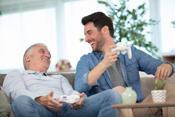 senior father with adult son relaxing on sofa at home