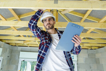 male worker holding a clipboard checking wood beams - Powered by Adobe