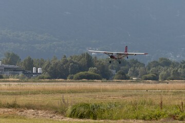 Fototapeta na wymiar White Aircraft plane landing on grass meadows with trees under blue sky