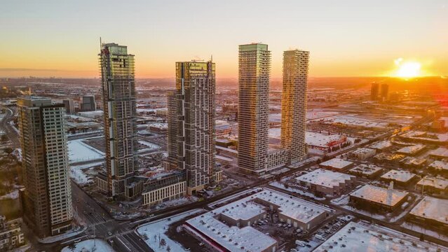 Drone time-lapse view over illuminated high-rise buildings by industrial buildings in the sunset