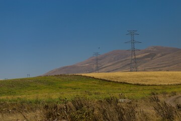 Electric pylons in large green hills and plains under blue sky