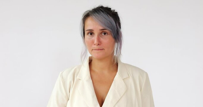 Young woman feels guilty about the mistake, worries and listens to the criticism. Portrait of one woman with colored hair on white background. She hides her gaze and tightens her lips