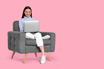 Fototapeta na wymiar Happy woman with laptop sitting in armchair on pink background