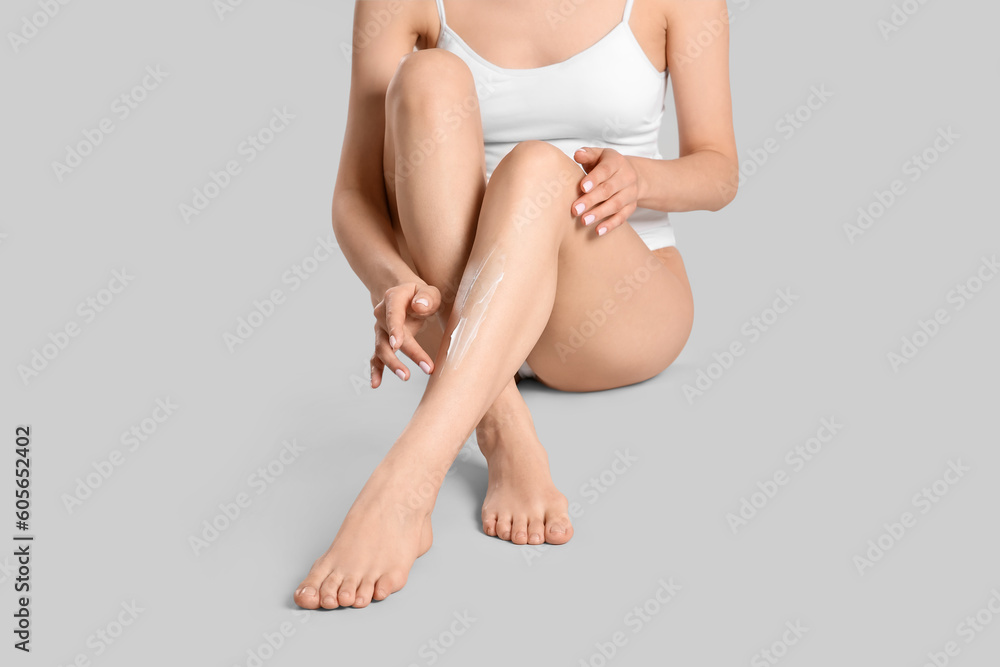 Canvas Prints Woman applying body cream onto her smooth legs on light grey background, closeup