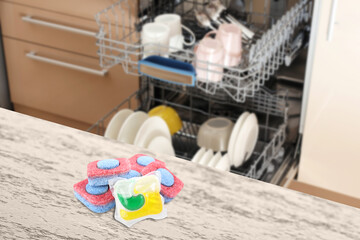 Dishwasher detergent pod and tablets on white wooden table in kitchen