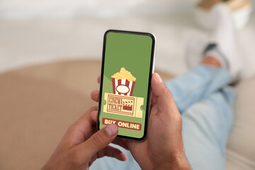 Man buying cinema tickets online via mobile phone at home, closeup