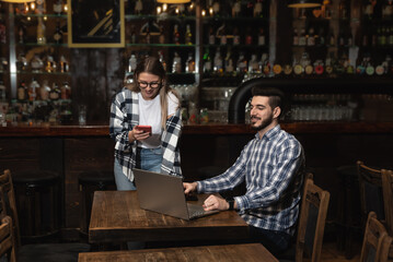 Two Diverse Entrepreneurs Have a Team Meeting in Their Stylish Coffee Shop. Barista and Cafe Owner Discuss Work Schedule and Menu on Laptop Computer. Multiethnic Female and Male Restaurant Employees.