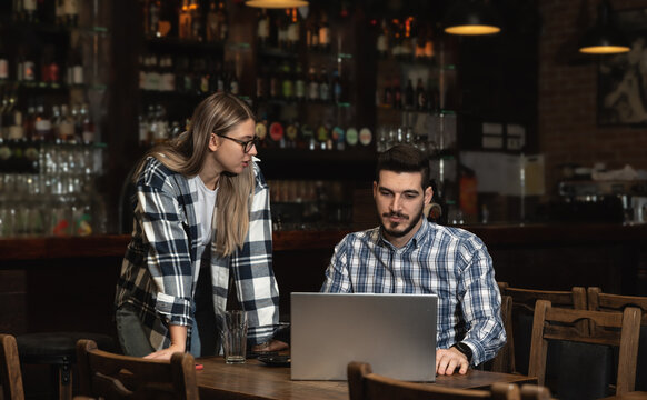 Two Diverse Entrepreneurs Have a Team Meeting in Their Stylish Coffee Shop. Barista and Cafe Owner Discuss Work Schedule and Menu on Laptop Computer. Multiethnic Female and Male Restaurant Employees. - Powered by Adobe