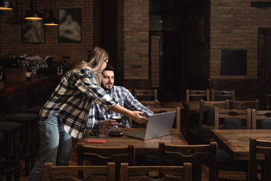Two Diverse Entrepreneurs Have a Team Meeting in Their Stylish Coffee Shop. Barista and Cafe Owner Discuss Work Schedule and Menu on Laptop Computer. Multiethnic Female and Male Restaurant Employees.