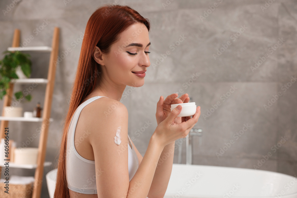 Wall mural beautiful young woman applying body cream onto shoulder in bathroom, space for text