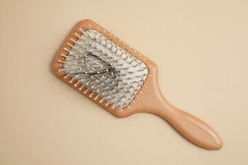 Wooden brush with lost hair on beige background, top view