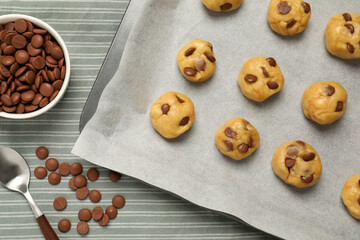 Fototapeta premium Baking pan with unbaked cookies and chocolate chips on tablecloth, flat lay
