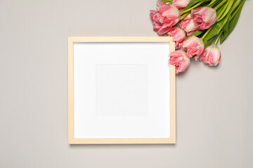 Empty photo frame and beautiful tulip flowers on light gray background, flat lay. Mockup for design
