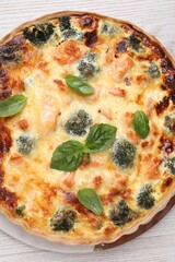 Delicious homemade quiche with salmon, broccoli and basil leaves on table, top view