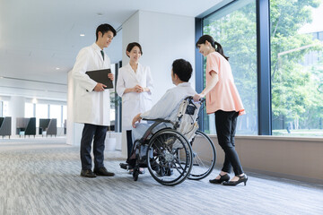大きな病院で介護や看護される車いすに乗った男性とドクターと看護師の様子