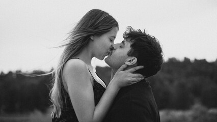 Romantic couple in love hugging and kissing in black and white photography with noise effect. Couple of young lovers giving each other a big kiss of romantic love with a landscape in the background