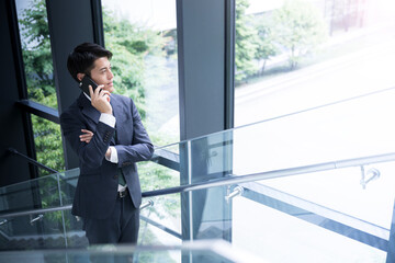Cool Asian businessman thinking and talking on his phone on the stairs of a beautiful office.