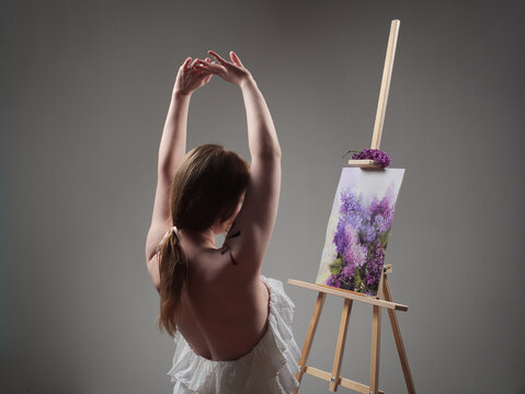 beautiful girl artist in the studio in a light dress with bare shoulders at the easel