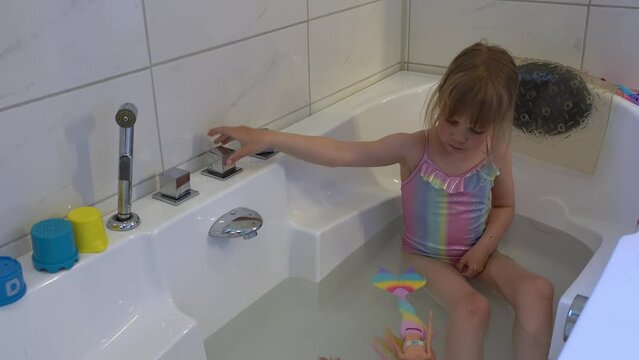 Young girl wearing swimsuit in bathtub turns water off then back on.