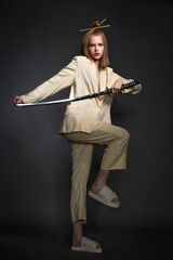 a beautiful girl with a beautiful figure in a light suit and a Japanese sword in her hands pose standing in the studio on a dark background