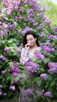 Young pretty woman enjoys by blooming lilac shrubs in garden.