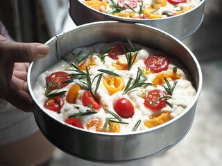round focaccia bread dough with rosemary, red and yellow cherry tomato and olive oil