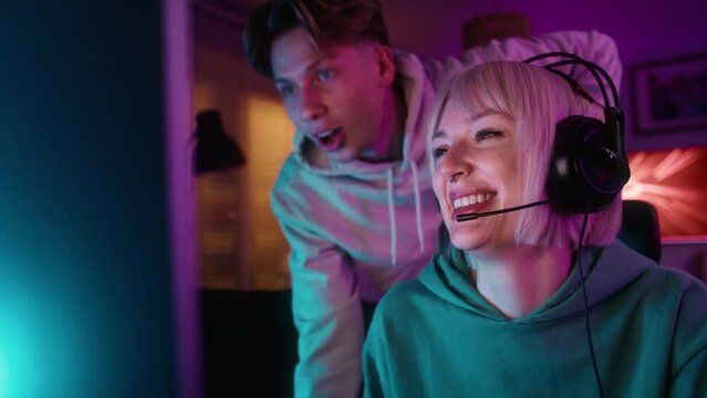 Caucasian woman playing game at night on Desktop PC and her friend is supporting her. Shot with RED helium camera in 8K.  